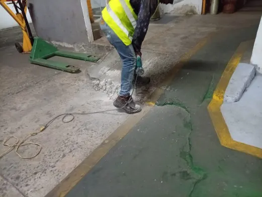 Operario con chaleco reflectivo reparando el piso de un área de producción